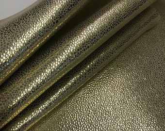 May include: Close-up of a gold textured leather fabric. The fabric has a pebbled surface and a metallic sheen.