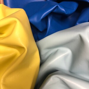May include: Close-up of four pieces of leather in different colors: yellow, light blue, dark blue, and a light brown. The leather is folded and textured.