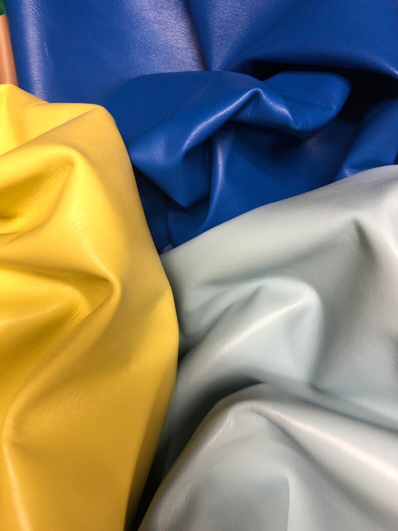 May include: Close-up of four pieces of leather in different colors: yellow, light blue, dark blue, and a light brown. The leather is folded and textured.
