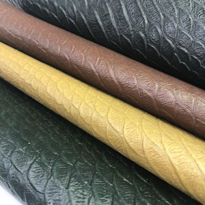 May include: Close-up of four different colors of faux leather fabric with a textured, scaly pattern. The colors are black, brown, beige, and green.