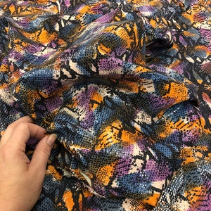 May include: A close-up of a fabric with a snakeskin pattern in shades of blue, orange, purple, and black.
