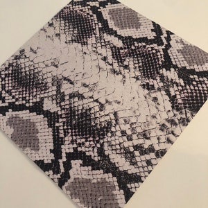 May include: A close-up of a white and black snakeskin pattern fabric. The fabric has a textured surface and a subtle pink hue.