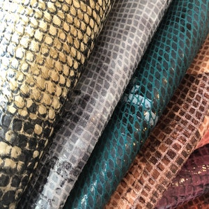 May include: Close-up of four different types of snakeskin fabric. The fabric is in various shades of brown, gray, teal, and black. The fabric has a textured, scaly pattern.