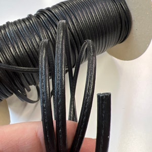 May include: Black leather cord with a smooth, slightly textured finish. The cord is wound around a cardboard spool.