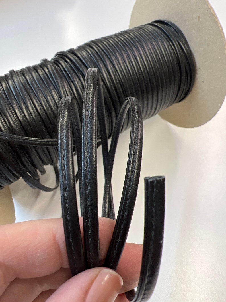 May include: Black leather cord with a smooth, slightly textured finish. The cord is wound around a cardboard spool.