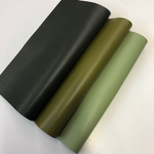 May include: Three pieces of leather in different shades of green and black. The leather is folded and stacked on top of each other.