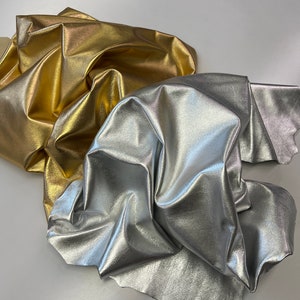 May include: Two pieces of fabric, one gold and one silver, are crumpled together. The fabric has a metallic sheen.