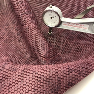 May include: Close-up of a piece of textured, mauve-colored leather. A silver dial gauge measures the thickness of the material. The leather has a repeating, scale-like pattern. Text on the gauge reads "GALATI MADE IN ITALY".