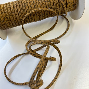 May include: A spool of brown suede cord with a black leopard print pattern. The cord is wound around a white cardboard spool.