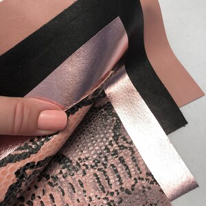 May include: Four pieces of leather in different textures and colors. The top piece is a light pink, the second is black, the third is a metallic rose gold, and the bottom piece is a pink snakeskin pattern.