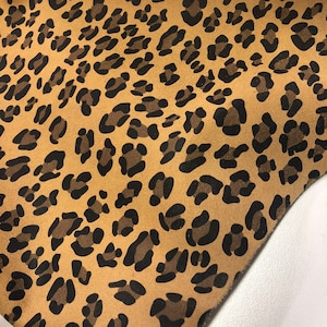 May include: A close-up of a brown fabric with a black leopard print pattern.