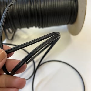 May include: A spool of black leather cord, with a close-up of the cord showing its texture and stitching.