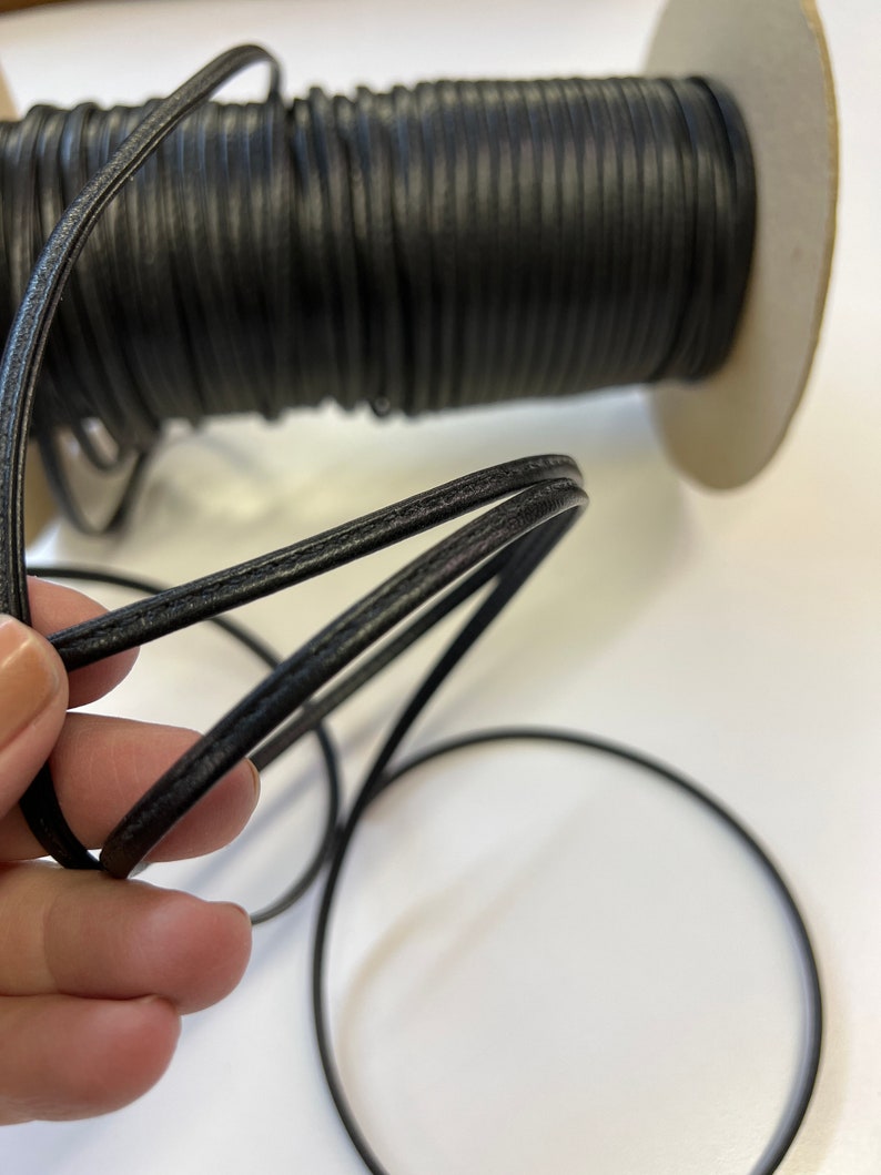 May include: A spool of black leather cord, with a close-up of the cord showing its texture and stitching.