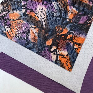 May include: Three fabric swatches, one with a purple, orange, and blue snake skin pattern, one with a white textured surface, and one with a purple textured surface.