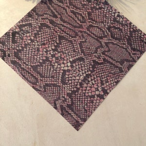 May include: A close-up of a pink and black snakeskin patterned fabric. The fabric has a textured surface and a subtle sheen.