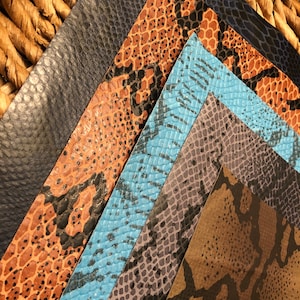 May include: An assortment of faux leather sheets in various colors and snake skin patterns. The colors include black, orange, blue, gray, and brown. The sheets are arranged in a fan shape, showcasing the different textures and designs.