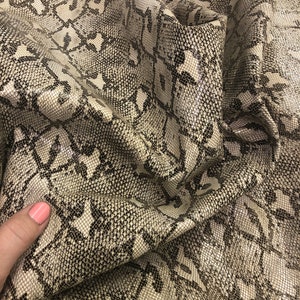 May include: Close-up of a beige and black snakeskin fabric with a geometric pattern. The fabric is textured and has a slight sheen.