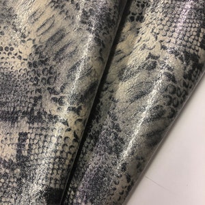 May include: Close-up of a silver and black fabric with a snakeskin pattern. The fabric has a glittery finish.