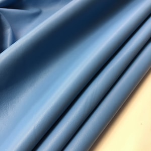 May include: A close-up of a light blue leather fabric. The fabric is folded and has a smooth, textured surface.