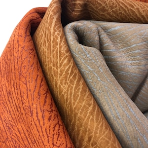 May include: Three pieces of leather in different shades of brown, orange, and blue. The leather has a textured surface with a pattern of lines.