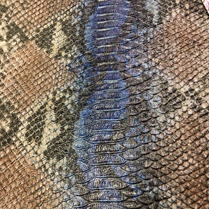 K&ouml;nnte beinhalten: Nahaufnahme eines Schlangenlederstoffs mit einem braunen und schwarzen Muster auf der linken Seite und einem blauen und schwarzen Muster auf der rechten Seite.