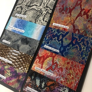 May include: A collection of eight different snake skin patterned fabric swatches. The swatches are labeled with their color and pattern names: Light Beige/Black, Metallic Multi Red, Metallic Blue/Aqua/Silver, Grey Suede, Metallic Multi Blue, Metallic Multi Orange, Gold/Silver/Bronze, and Blue/Purple/Orange/Black.