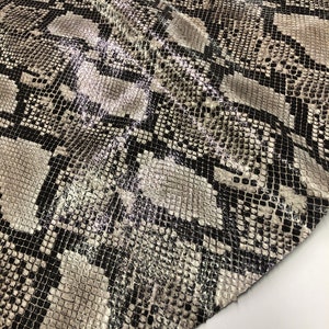 May include: Close-up of a black and white snakeskin fabric with a textured pattern. The fabric is folded in half and the edges are visible.