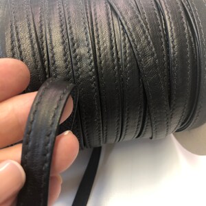 May include: Black leather cord with a stitched edge. The cord is rolled up on a spool.