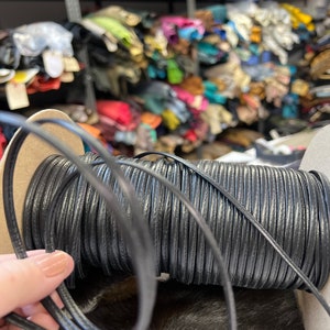 May include: A spool of black leather cord, wound tightly and ready for crafting projects. The cord is smooth and supple, perfect for making jewelry, belts, or other leather goods.