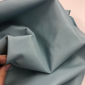 May include: A close-up of a light blue leather fabric. The fabric is folded and textured.
