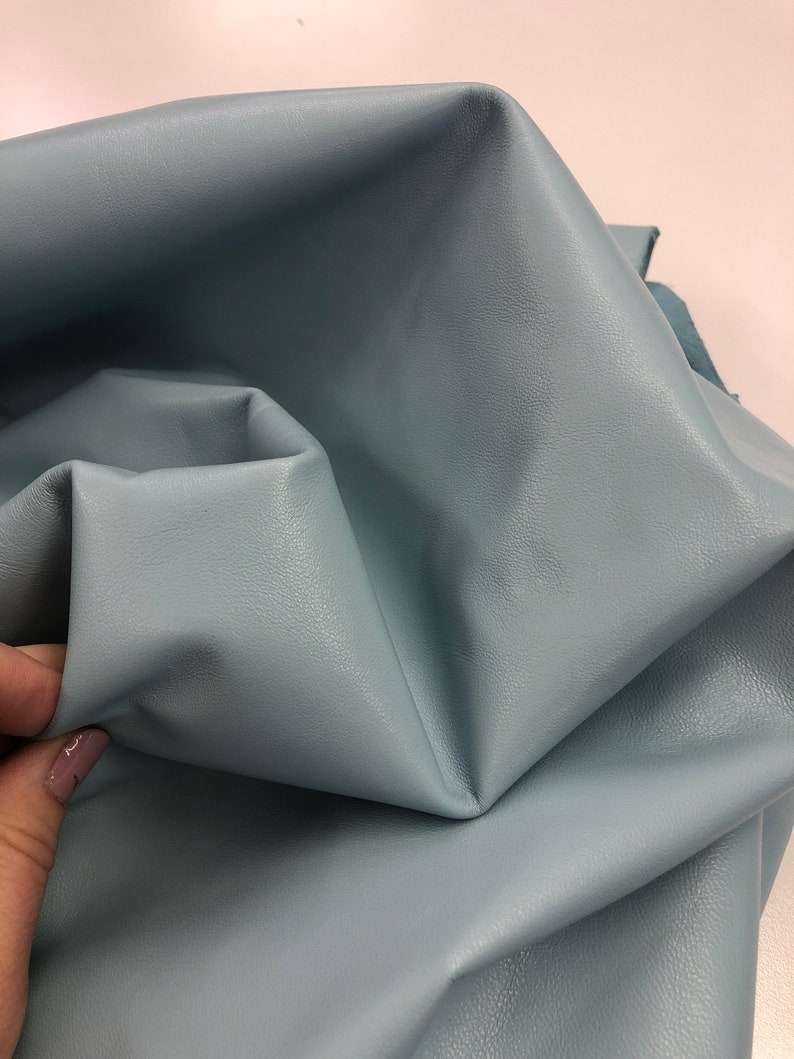 May include: A close-up of a light blue leather fabric. The fabric is folded and textured.