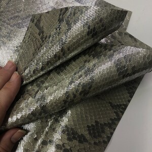May include: A piece of silver metallic fabric with a snakeskin pattern. The fabric is folded in half and has a subtle sheen.