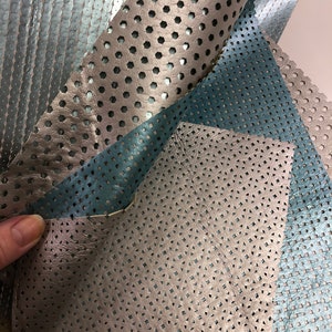 May include: Close-up of three pieces of perforated leather in different colors and patterns. The leather is a light brown, a dark blue, and a silver color. The leather has a variety of different hole patterns.