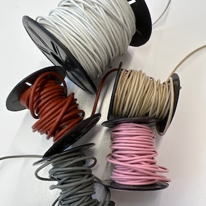 May include: Five spools of leather cord in different colors: white, brown, red, pink, and gray. The spools are all on a white surface.