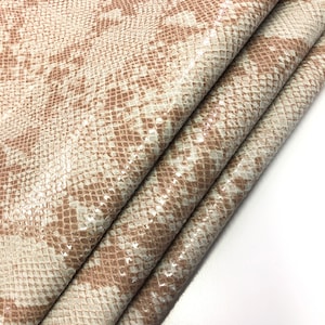 May include: Close-up of a beige snakeskin fabric with a subtle shimmer. The fabric is folded in thirds, showing the texture and pattern.