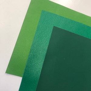 May include: Three sheets of green leather in different shades of green. The top sheet is a light green, the middle sheet is a medium green, and the bottom sheet is a dark green.