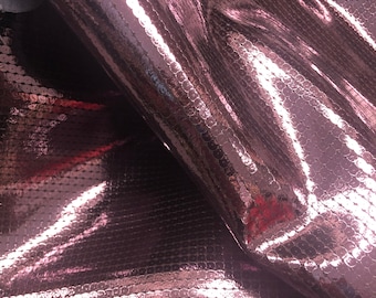 May include: Close-up of a shiny, rose-colored fabric covered in small, round sequins. The fabric is folded, creating shadows and highlights that emphasize the texture and reflective quality of the sequins. The overall effect is glamorous.