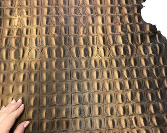 May include: A close-up of a brown alligator skin with a textured pattern. The skin is smooth and has a slight sheen.