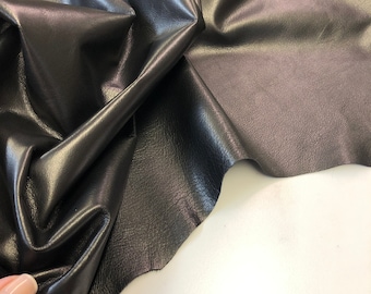 May include: Black leather fabric with a smooth, shiny finish. The fabric is folded and draped on a white surface.