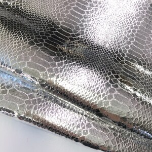 May include: Close-up of a silver snakeskin-embossed fabric with a textured, shiny finish.