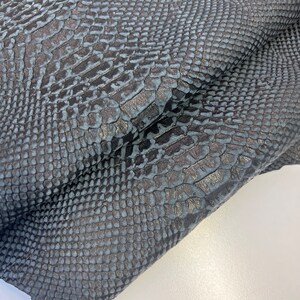 Puede incluir: Primer plano de una tela de piel de serpiente azul oscuro con un patr&oacute;n texturizado y escamoso.