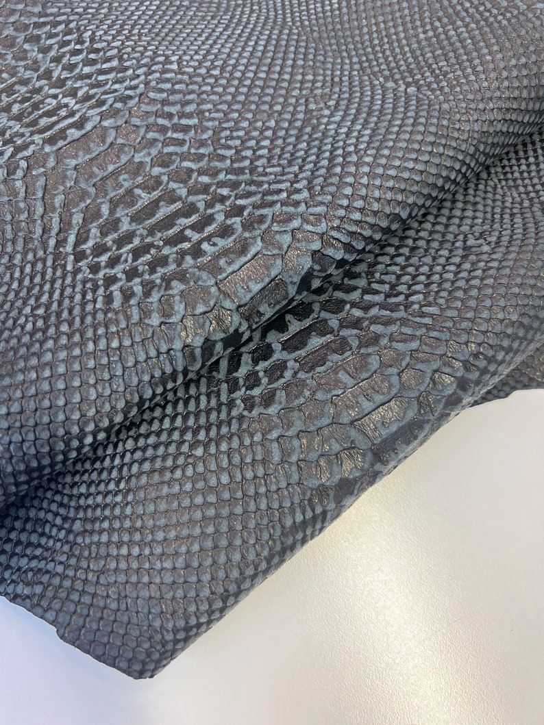 Puede incluir: Primer plano de una tela de piel de serpiente azul oscuro con un patr&oacute;n texturizado y escamoso.