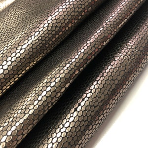 May include: Close-up of a black snakeskin-embossed fabric with a metallic silver finish. The fabric is folded in thirds, showing the texture and sheen.