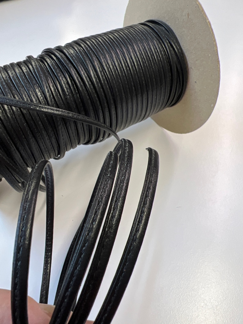 May include: A spool of black leather cord with a textured surface. The cord is wound around a cardboard spool.