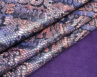 May include: Purple and silver snakeskin fabric with a textured surface. The fabric is folded over itself and the bottom edge is on a purple background.