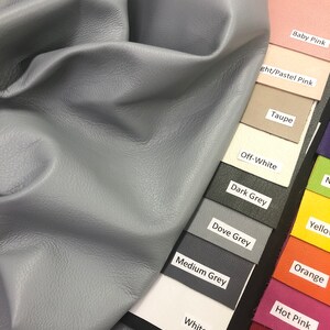 May include: A close-up of a light blue leather swatch, displayed against a color chart with various shades of gray, white, pink, orange, yellow, and red. The color chart includes the names of each color, such as "Baby Pink", "Taupe", "Off-White", "Dark Grey", "Dove Grey", "Medium Grey", "White", "Hot Pink", "Red", and "Orange".