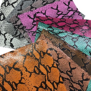 May include: Assortment of faux snakeskin fabric sheets in various colors, including brown, gray, pink, teal, and black. The sheets are arranged in a fan shape, with the brown sheet at the bottom.