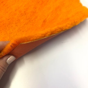 May include: A close-up of a bright orange faux fur fabric with a soft, fuzzy texture. The fabric is folded in half, revealing a smooth, orange backing.