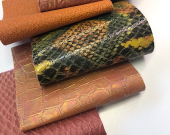 May include: Five different pieces of leather in various colors and textures. The leather is arranged in a stack, with the top piece being a dark brown with a floral pattern. The other pieces are a light brown with a textured surface, a green and yellow snakeskin pattern, a gold with a crocodile pattern, and a dark red with a textured surface.