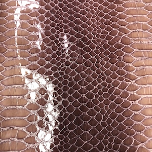 May include: Close-up of a textured, shiny, purple snakeskin fabric. The fabric has a repeating pattern of scales.